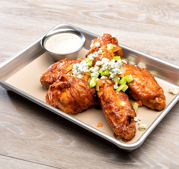 Buffalo chicken wings dressed with blue cheese shown on silver serving tray